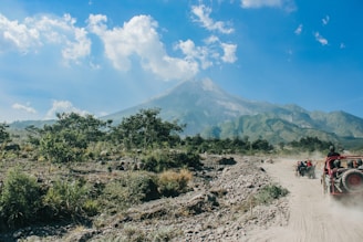 a jeep driving down a dirt road with a mountain in the background