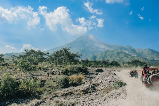 a jeep driving down a dirt road with a mountain in the background