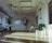 A spacious room with wooden flooring is filled with natural light streaming through large windows. A potted plant with wide, green leaves sits prominently on the floor. The walls are decorated with large speakers and a neon sign that reads 'We work for musicians'. A shiny disco ball and spotlights are visible on the ceiling, contributing to a modern and artistic vibe.