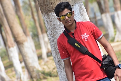 Model wearing a red stripe polo shirt walking through a sunlit park.