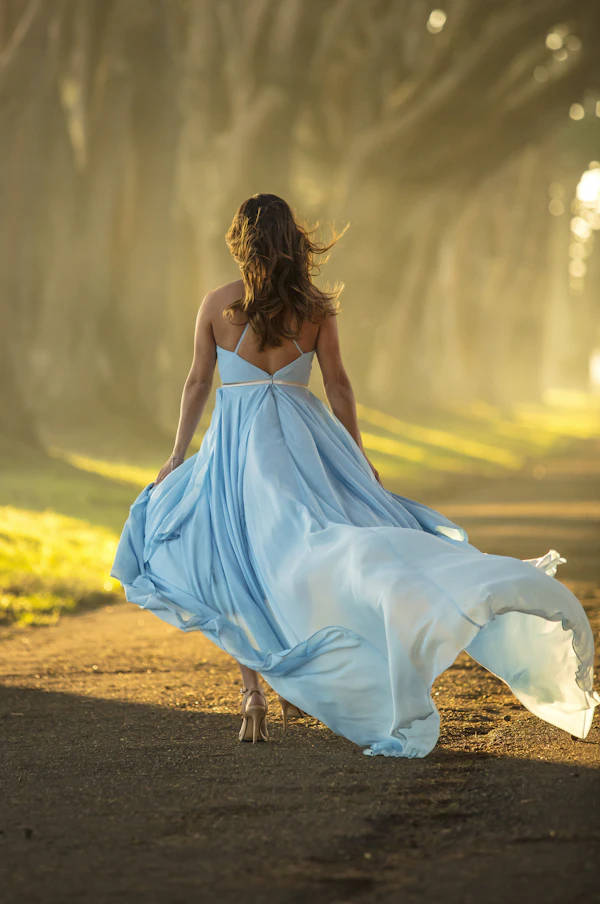 Woman in blue dress walking on road in warm sunlight