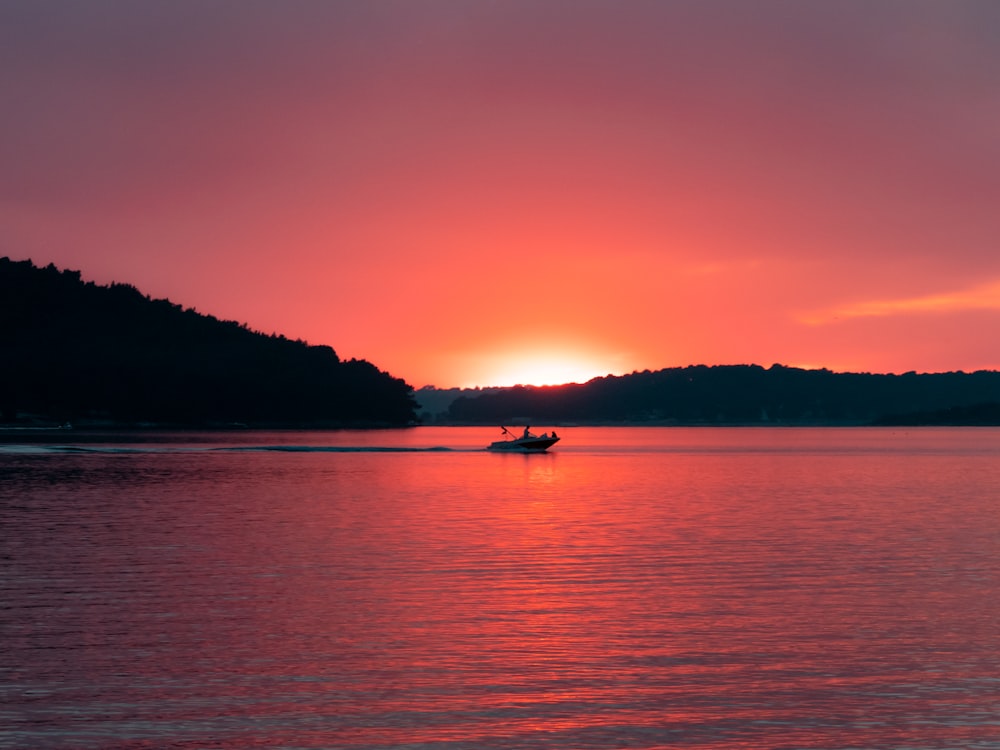 Homem no barco no mar ao pôr do sol com céu laranja