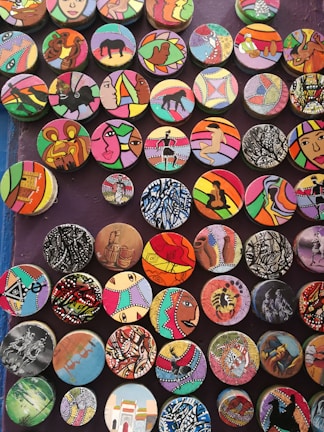 A collection of colorful, circular art pieces each featuring unique designs and patterns. The designs include abstract shapes, animals, people, and cultural motifs, with bold and varied color schemes.