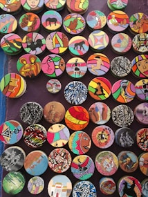 A collection of colorful, circular art pieces each featuring unique designs and patterns. The designs include abstract shapes, animals, people, and cultural motifs, with bold and varied color schemes.