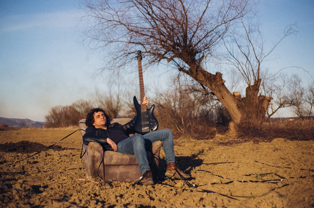 man sitting on sofa chair with electric guitar near bare tree