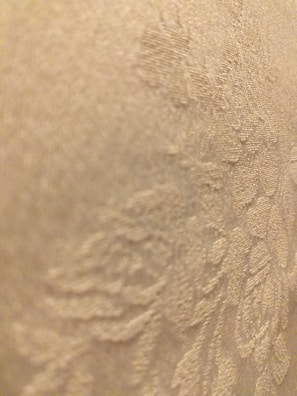 A close-up view of a textured fabric with a floral pattern. The surface appears to be soft and intricately woven.