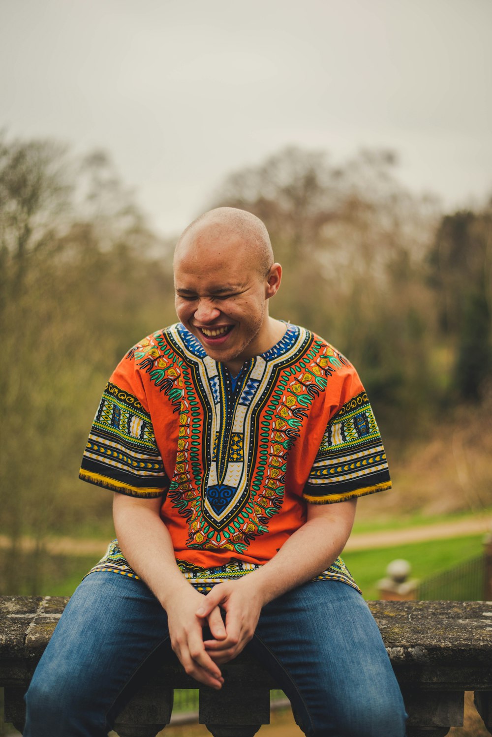 Uomo sorridente che indossa una camicia daishiki arancione e verde seduta su una superficie grigia