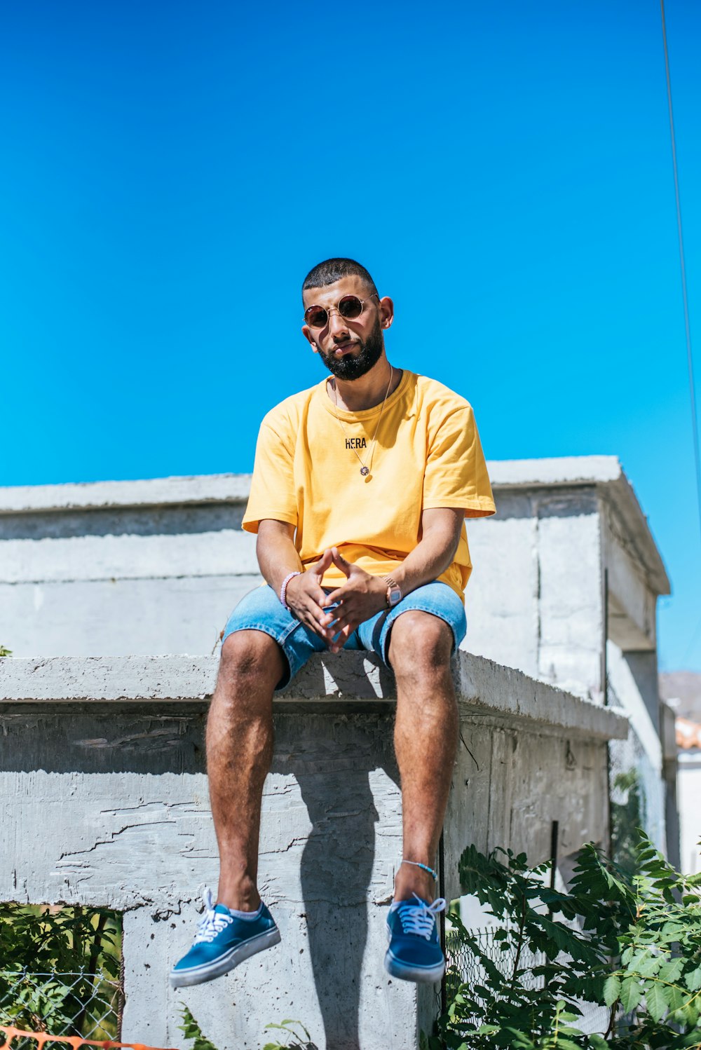 man wearing yellow crew-neck t-shirt sitting on white concrete pavement