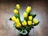 Bright yellow tulips arranged in a clear glass vase on a wooden table.