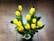 Bright yellow tulips arranged in a clear glass vase on a wooden table.