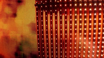 A vibrant display of vertical LED light strips emitting orange and red hues with a warm, glowing effect. The light patterns create a dynamic and colorful visual, resembling a digital or electronic art installation.