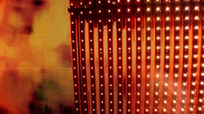 A vibrant display of vertical LED light strips emitting orange and red hues with a warm, glowing effect. The light patterns create a dynamic and colorful visual, resembling a digital or electronic art installation.