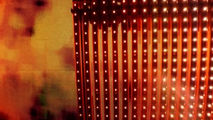 A vibrant display of vertical LED light strips emitting orange and red hues with a warm, glowing effect. The light patterns create a dynamic and colorful visual, resembling a digital or electronic art installation.