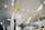 A modern airport interior with high ceilings and perforated panels. There are directional signs, including a yellow sign for Gate 7. The space is well-lit with overhead lights, and features glass railings and plants. A Wi-Fi symbol is visible, indicating connectivity services.