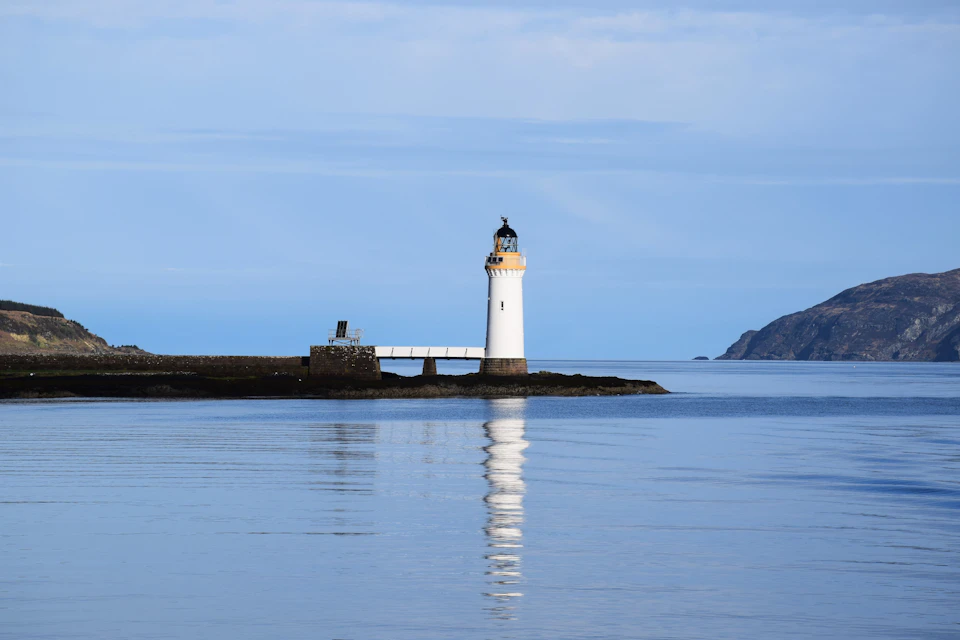 Lighthouse stands tall against deep blue ocean on rocky island with yellow roof