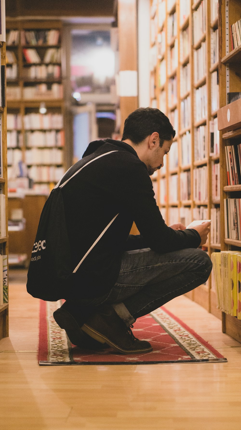 man squatting in front book shelves