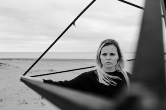 Black and white photo of a woman in elegant fitness wear standing on a sunlit beach with ocean waves in the background