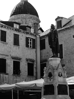 Historic photograph of a religious procession in a small Tuscan town square.