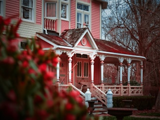 Elegant Victorian house painted in soft pastel pink with intricate white detailing on the porch.