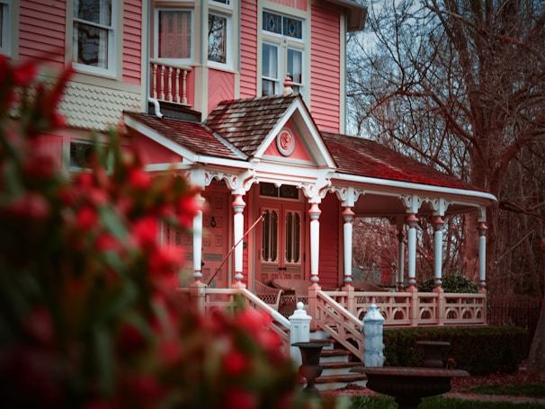 Elegant Victorian house painted in soft pastel pink with intricate white detailing on the porch.