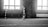 A child wearing a sports uniform stands on an indoor football field, one foot on a soccer ball. The background features a goalpost and large windows, allowing natural light to fill the space. The image is in black and white, which gives it a nostalgic and timeless feel.