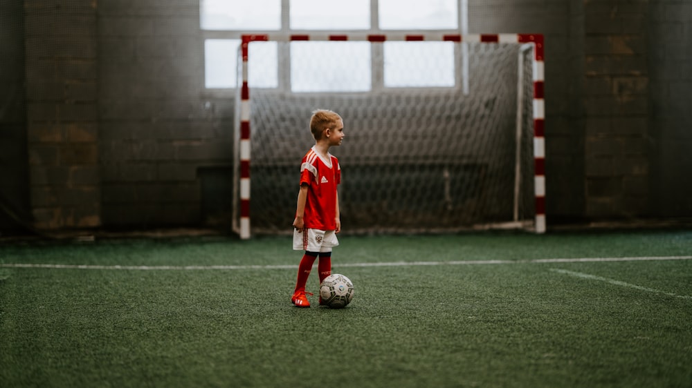 Menino em pé ao lado da bola de futebol perto da rede de futebol