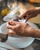 Hands using a modern kitchen gadget to peel fresh vegetables over a bright sink.