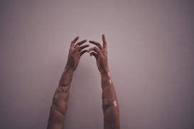 Two hands reaching upwards with arms partially covered in translucent tape against a plain background.