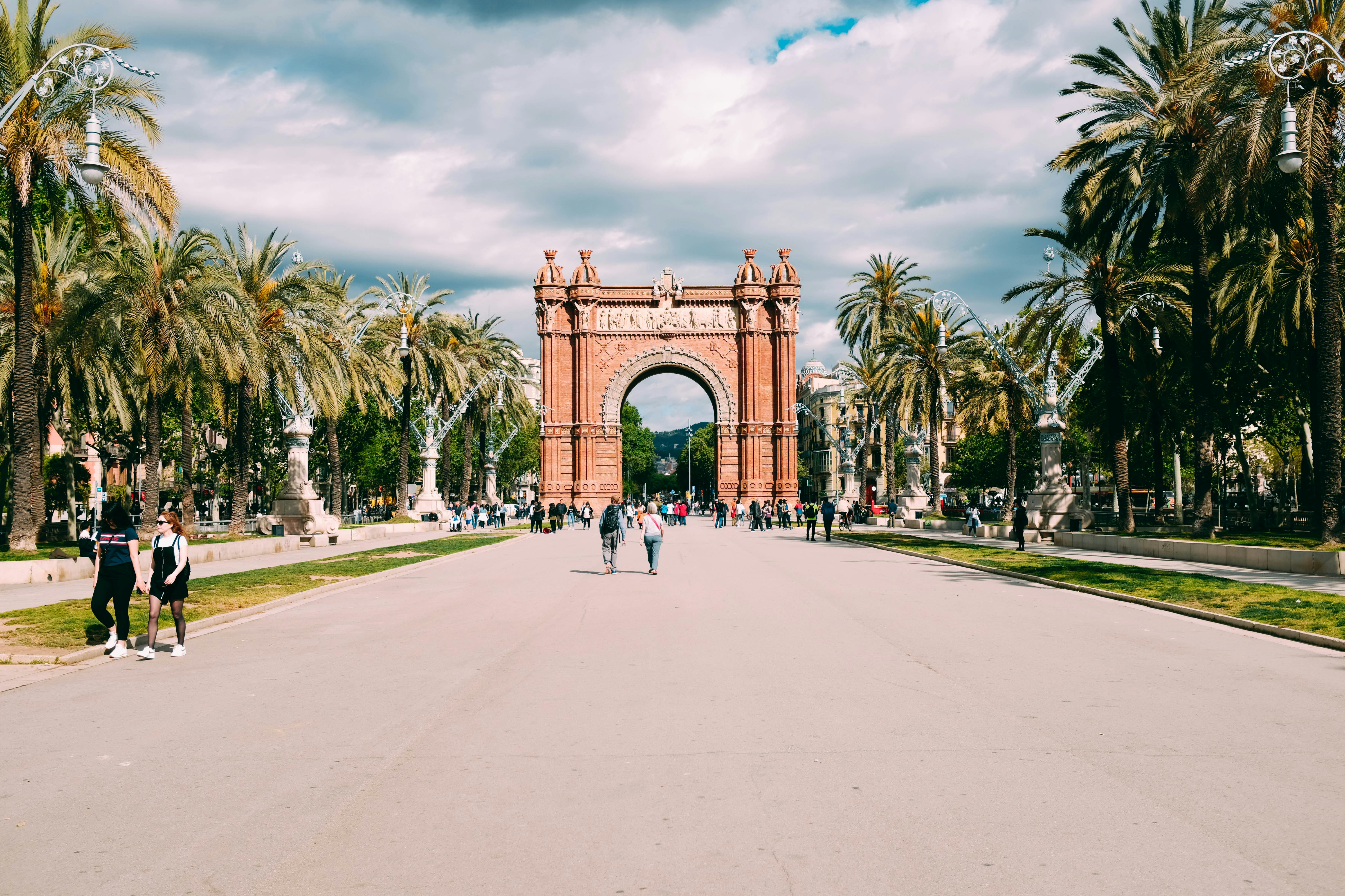 people walking near arc surrounded with tall and green trees under white and blue skies