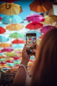 a woman holding a smart phone in front of colorful umbrellas