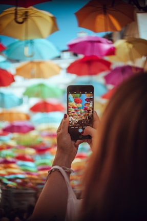a woman holding a smart phone in front of colorful umbrellas