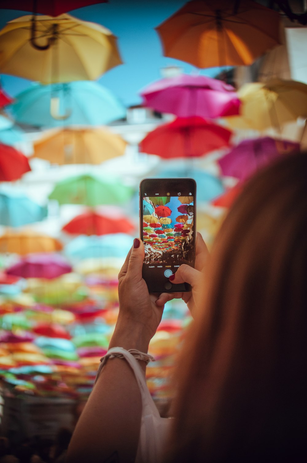 uma mulher segurando um telefone inteligente na frente de guarda-chuvas coloridos