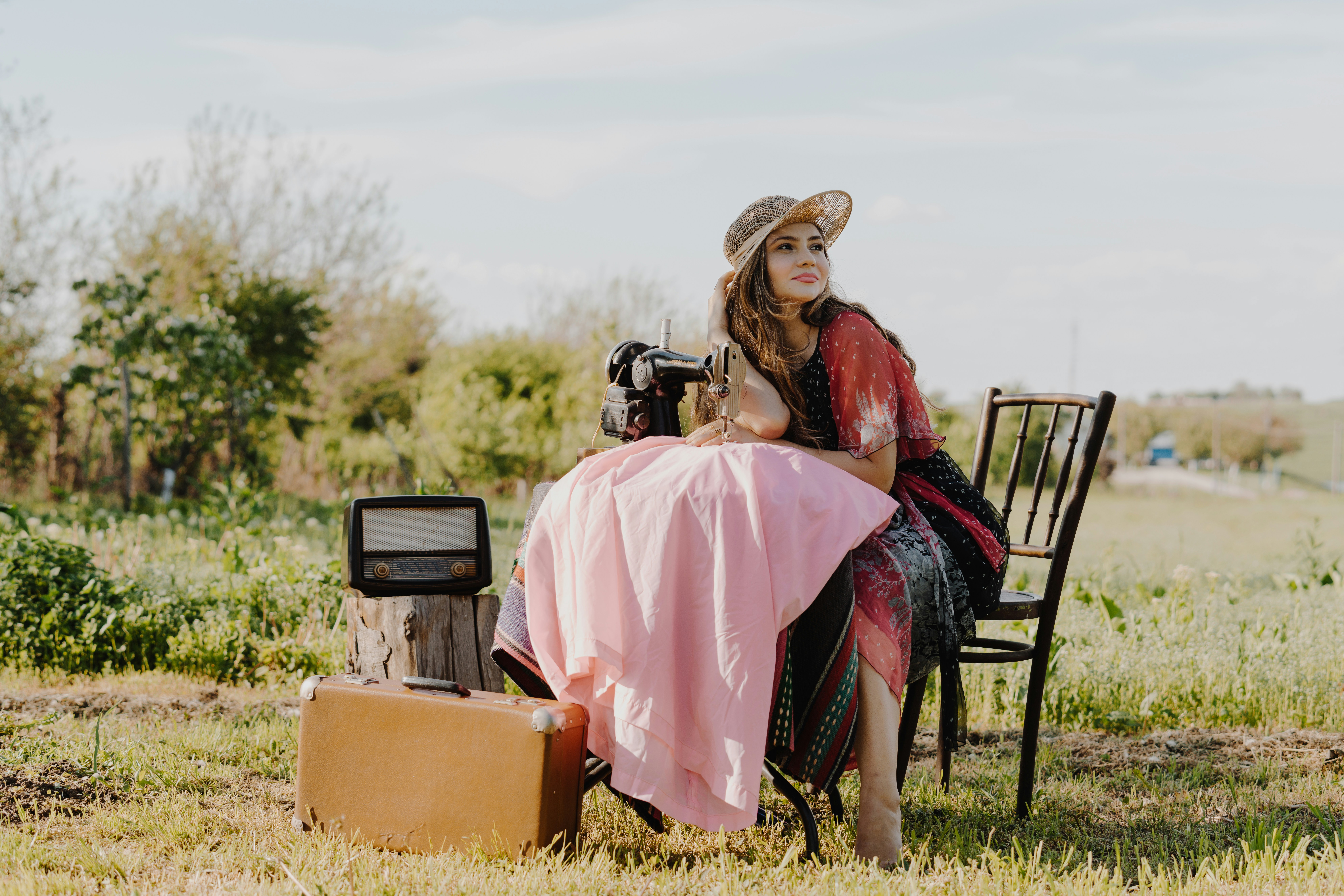 woman sitting on chair sewing near trees during daytime
