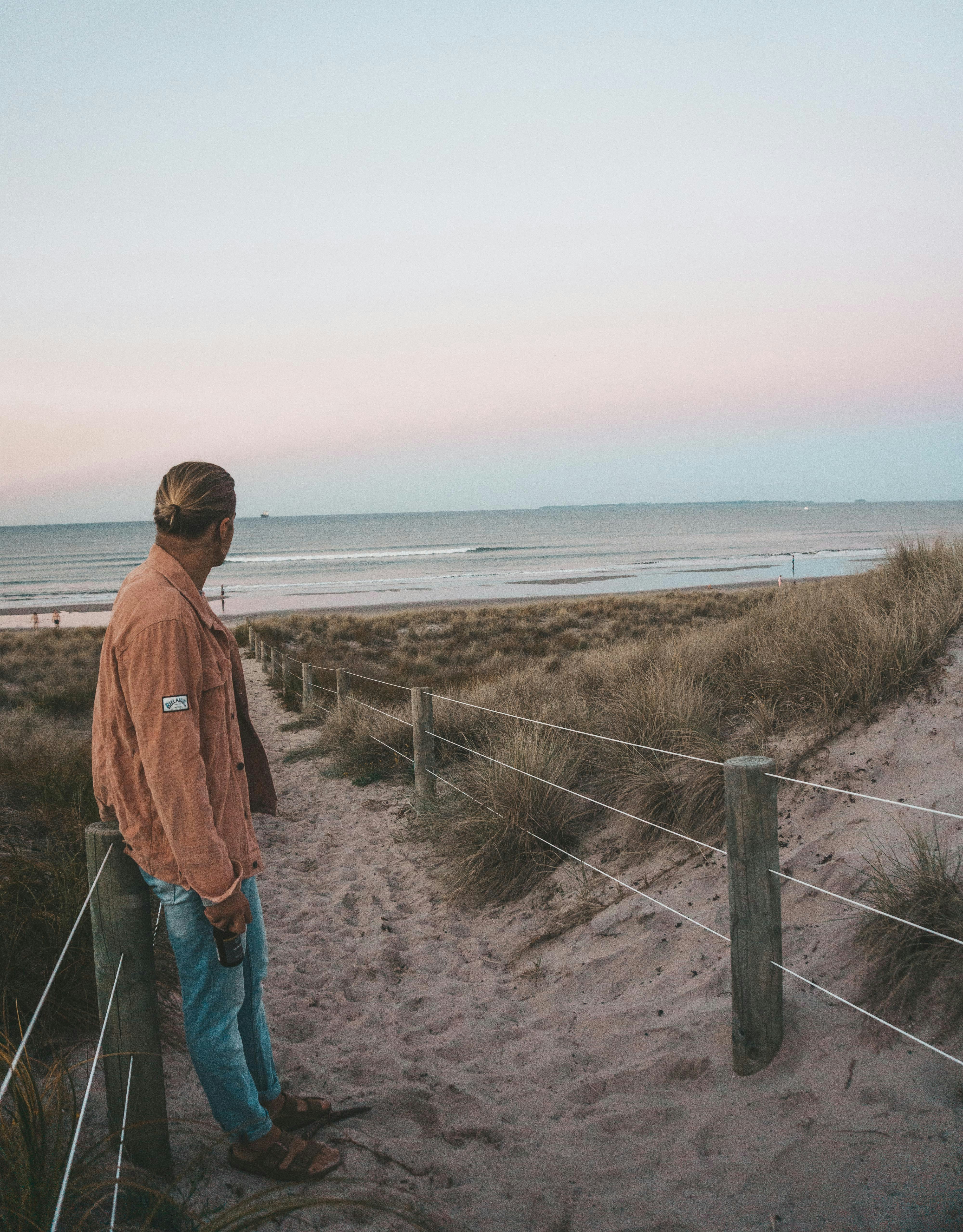 man in orange jacket standing at pathway towards shore