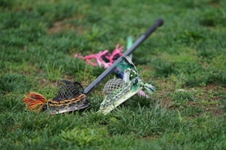 A close-up of a lacrosse stick resting on dark green and white team jerseys with the Methacton Warriors logo.