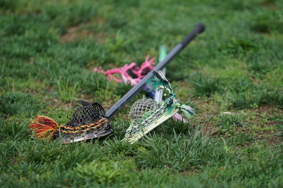 A close-up of a lacrosse stick resting on dark green and white team jerseys with the Methacton Warriors logo.