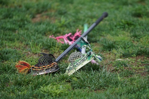 A close-up of a lacrosse stick resting on dark green and white team jerseys with the Methacton Warriors logo.