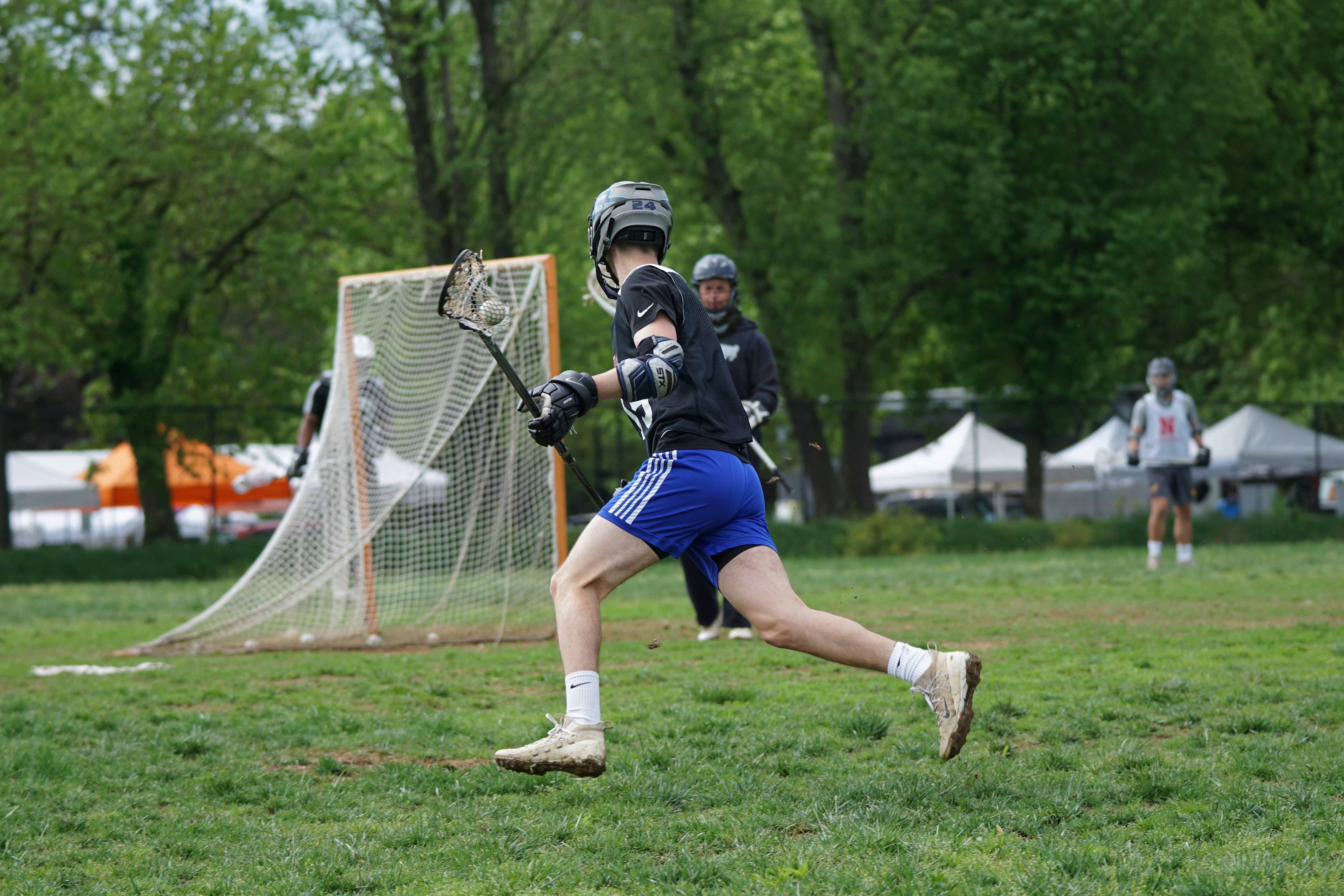 men playing lacrosse stick near trees at daytime