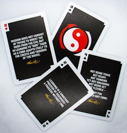 Four playing cards are arranged on a white surface. Each card contains a motivational quote attributed to Bruce Lee. The cards display different numbers and suits: hearts, clubs, and spades. One card features a red and white yin-yang symbol in the center.