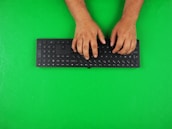 Close-up of hands typing on a keyboard with green and white branding visible.