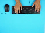 Close-up of hands typing on a keyboard with a blue and green color scheme in the background.