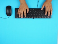 Close-up of hands typing on a keyboard with a minimalist navy blue and white theme background.