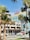 Palm trees frame a colorful hotel with a retro sign reading 'The Georgian'. Below, cars move along a busy street featuring a traffic light and a sidewalk with pedestrians. The sky is clear and blue.