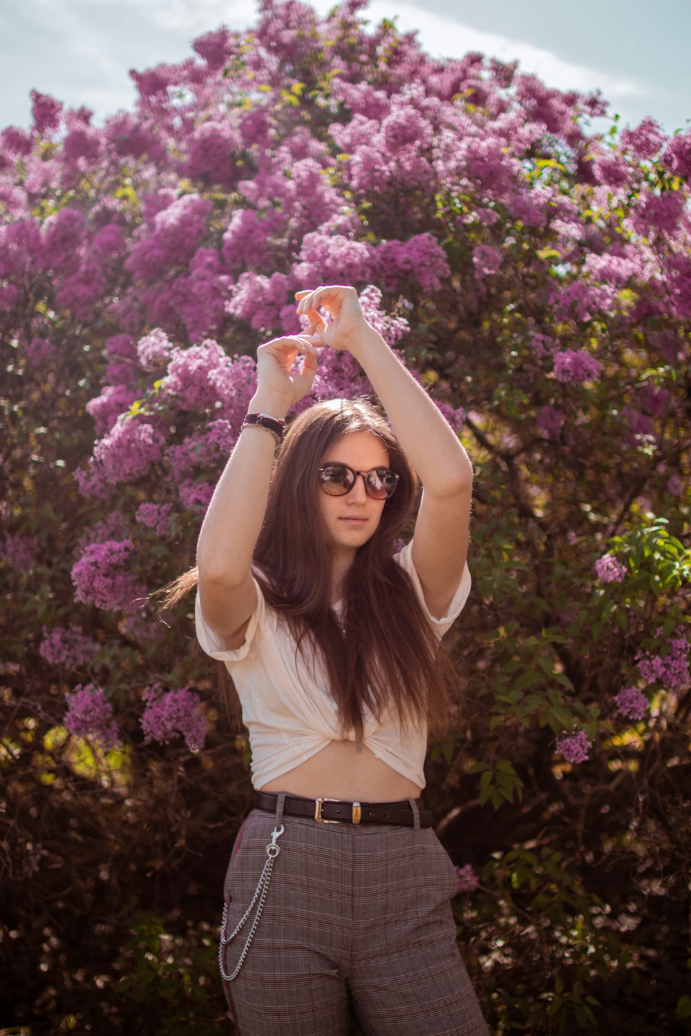 woman wearing white crop-top and gray pants beside purple petaled flower during daytime