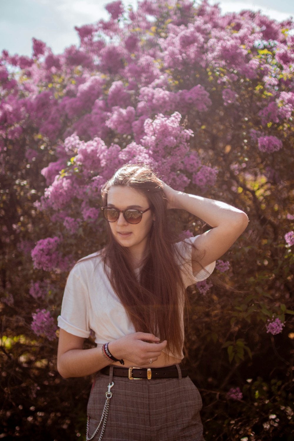 woman in white t-shirt wearing sunglasses standing beside purple flowers