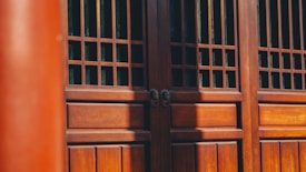 A detailed wooden structure with vertical and horizontal slats, possibly part of a traditional building element such as a door or window. The wood appears polished and is bathed in natural light, casting shadows across its surface.