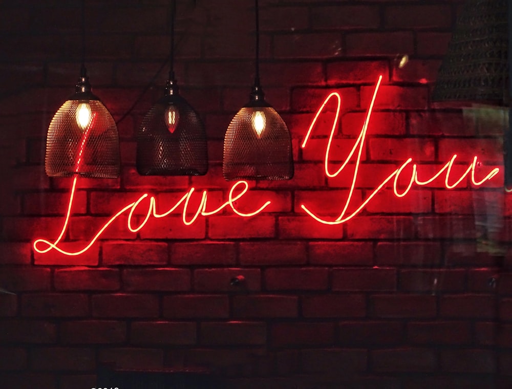 Trois lampes suspendues avec l’enseigne au néon Love You sur un mur de briques