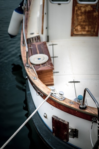 A close-up view of a wooden boat deck featuring a neatly coiled rope, with a boardwalk and a section of the boat railing visible. The water is dark and calm, suggesting a serene environment.