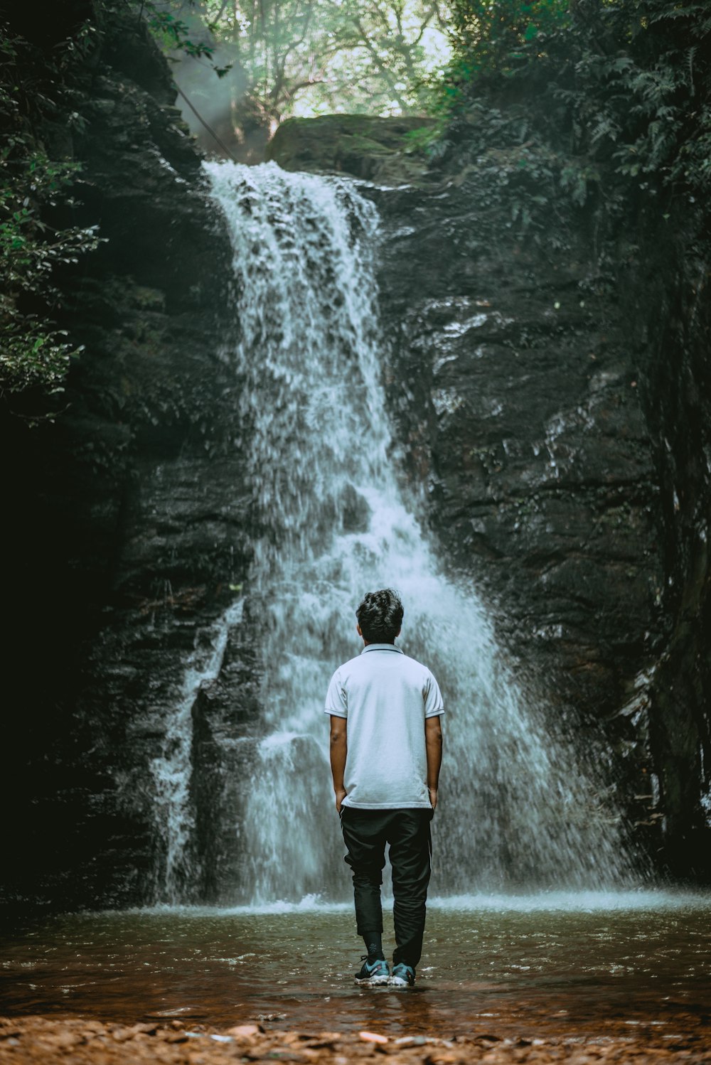 man wearing white shirt standing near waterfalls