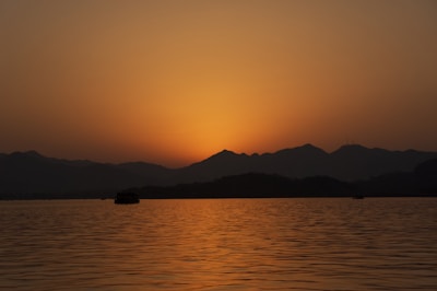 Sunset over the tranquil Kampot River with fishing boats silhouetted against the orange sky.